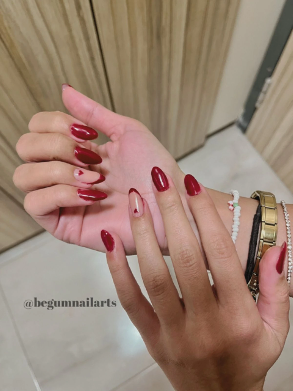 Dört tırnağında kırmızı protez tırnak olan ve yüzük tırnağında ten rengi üzerine kırmızı kalp ve french nail art uygulaması yapılmış bir kadının elleri