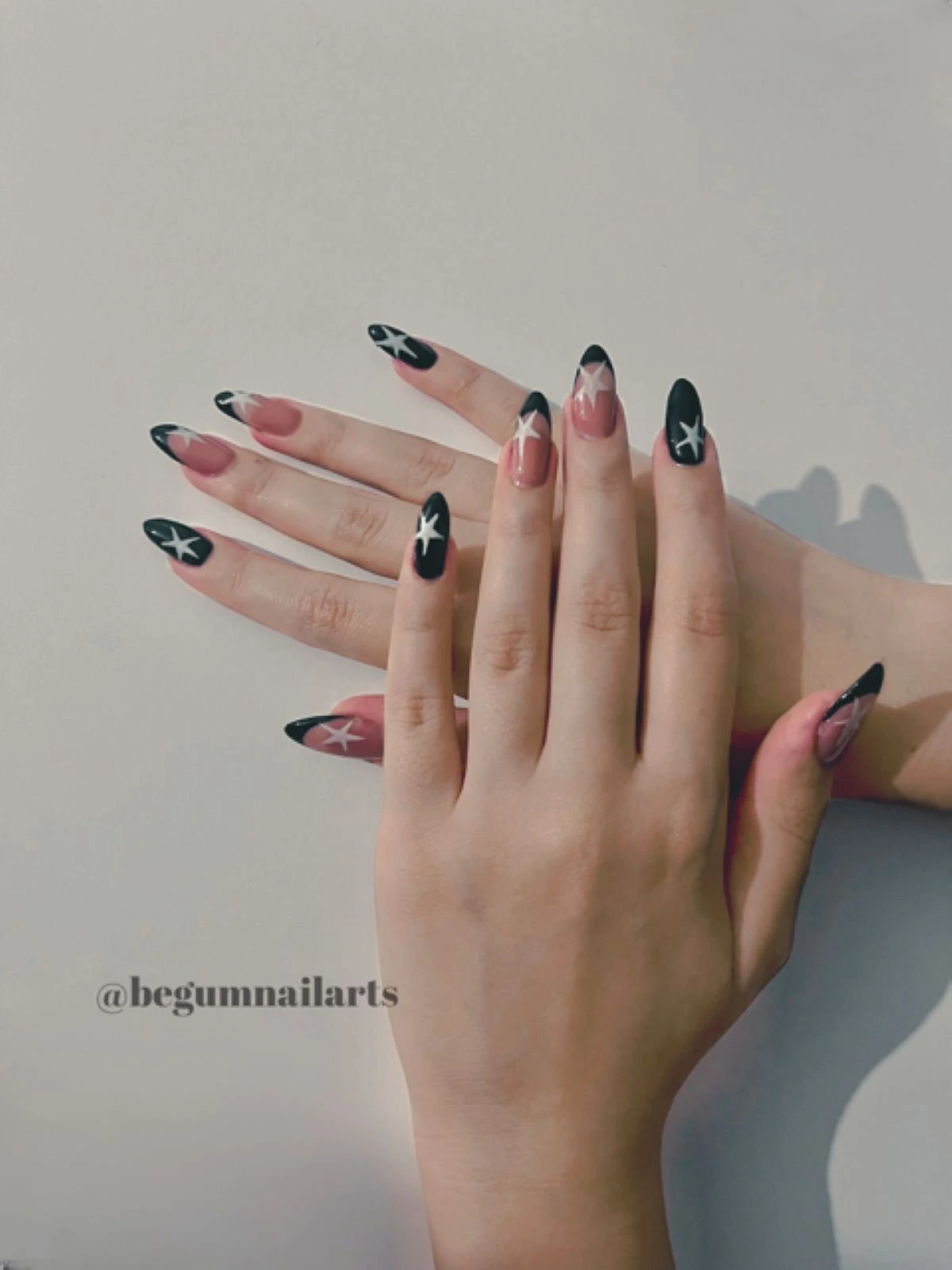 Serçe ve işaret tırnağında siyah üzerine yıldız, diğer parmaklarında pembe üzerine siyah french ve yıldız yapılmış bir kadının elleri