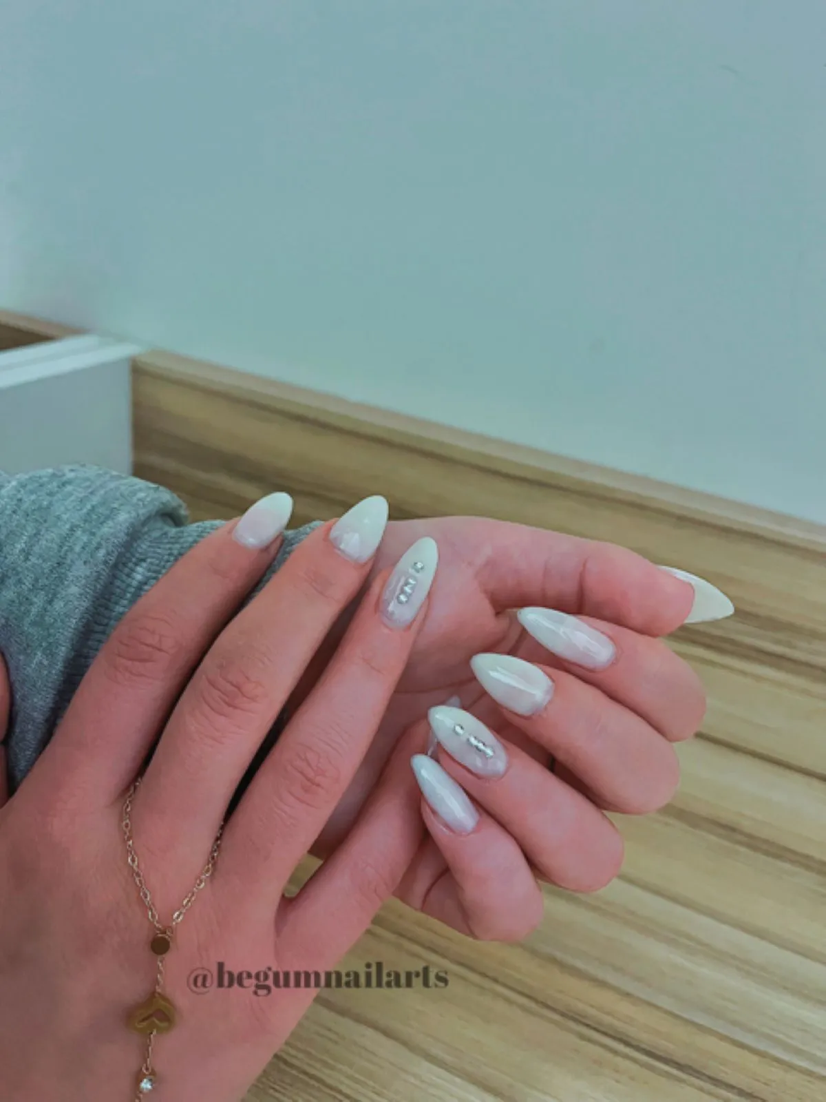 Rakı beyazı rengi uygulanmış protez tırnaklar ve yüzük tırnaklarında dikey olarak ışıltılı taşlar bulunan bir kadının elleri 