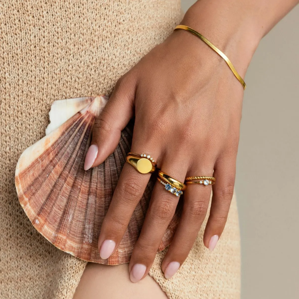 Elinde deniz kabuğu tutan, yüzükler takmış ve açık pembe oje sürülmüş bakımlı bir kadın eli.