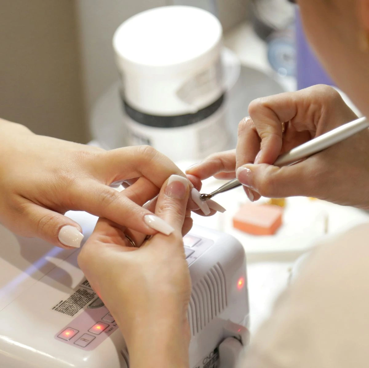 Bir tırnak uzmanı beyaz oje sürülmüş tırnakların üzerine fırça ile işlem yapıyor.