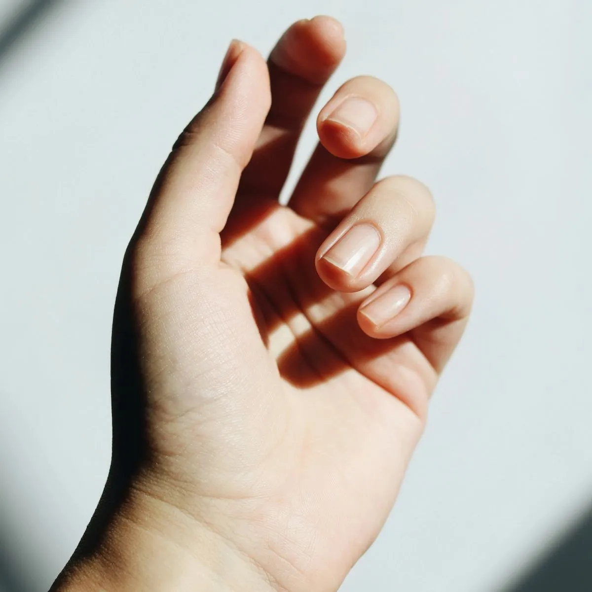 Arka planda beyaz ışığın olduğu temiz, oje sürülmemiş ve bakımlı tırnakları gösteren bir kadın eli